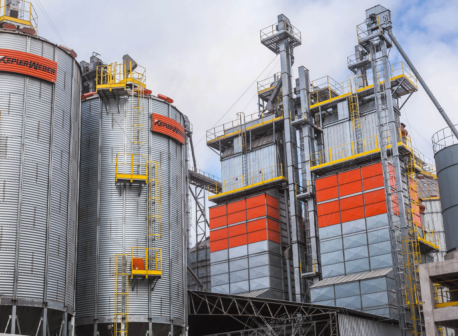 Uma plantação de grãos com 5 silos ao fundo, ao lado de um barracão.